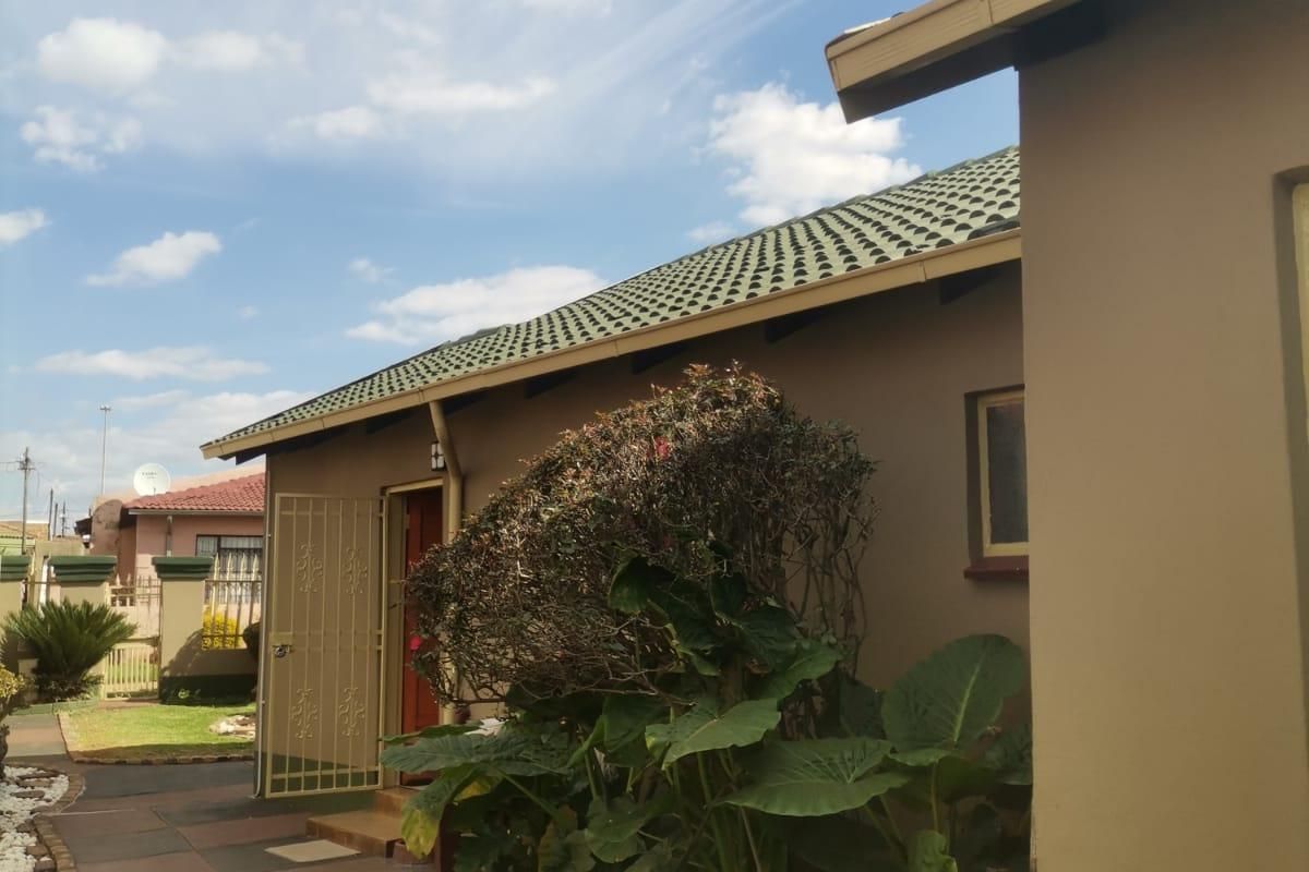 A view of the rear exterior of the house featuring a tiled roof, paved walkway, and security gate entrance.