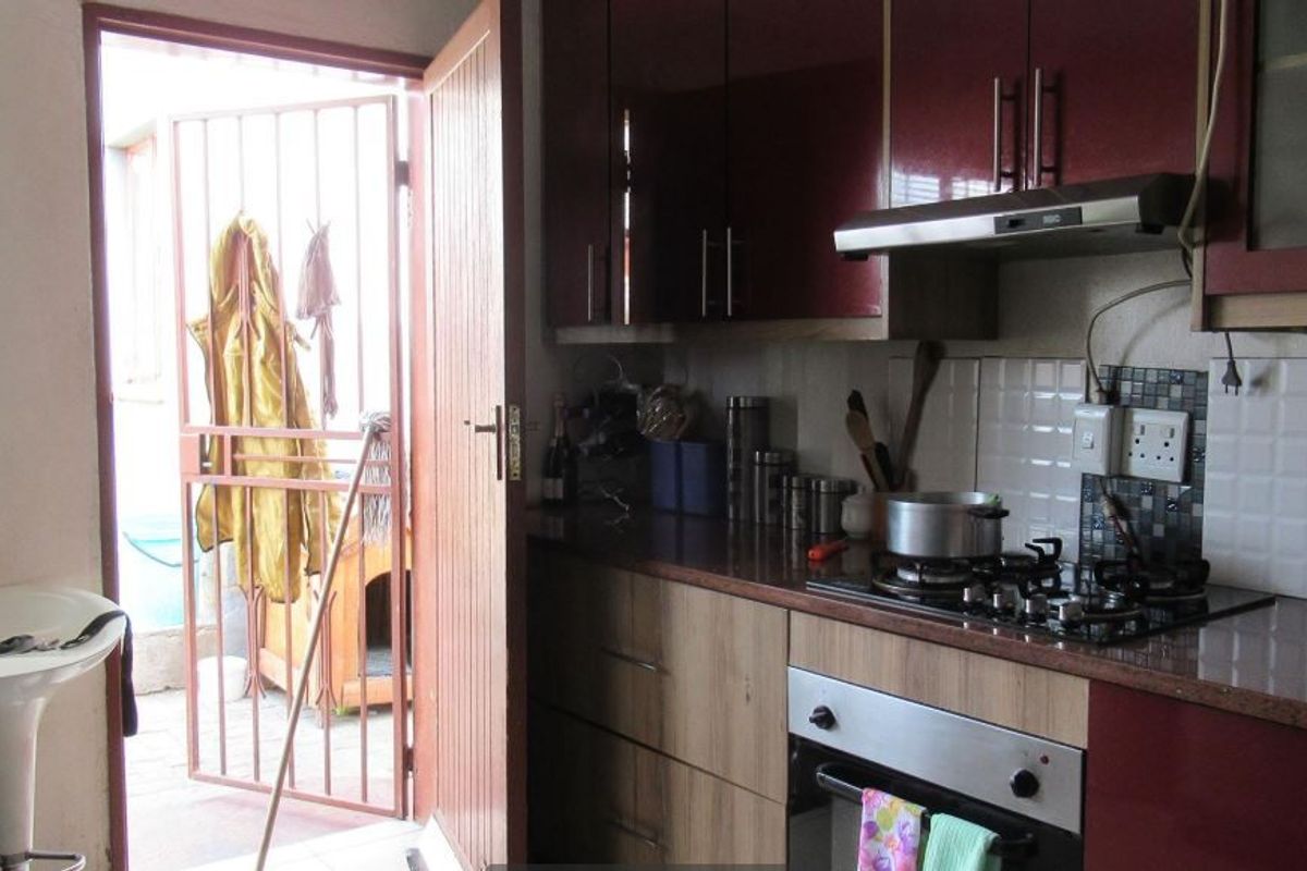 A functional kitchen featuring two-tone cabinetry, granite countertops, a gas hob, and an integrated oven, with direct access to an outdoor area.