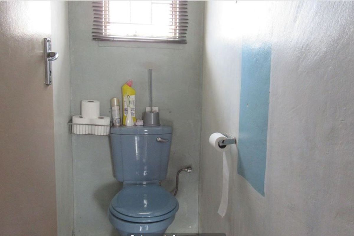 A compact bathroom featuring a blue toilet suite and a small window with blinds, requiring cosmetic updates to the wall finishes.