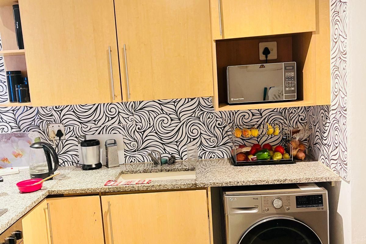Compact kitchen featuring light wood-finish cabinetry, granite countertops, a patterned tiled backsplash, and an integrated washing machine.
