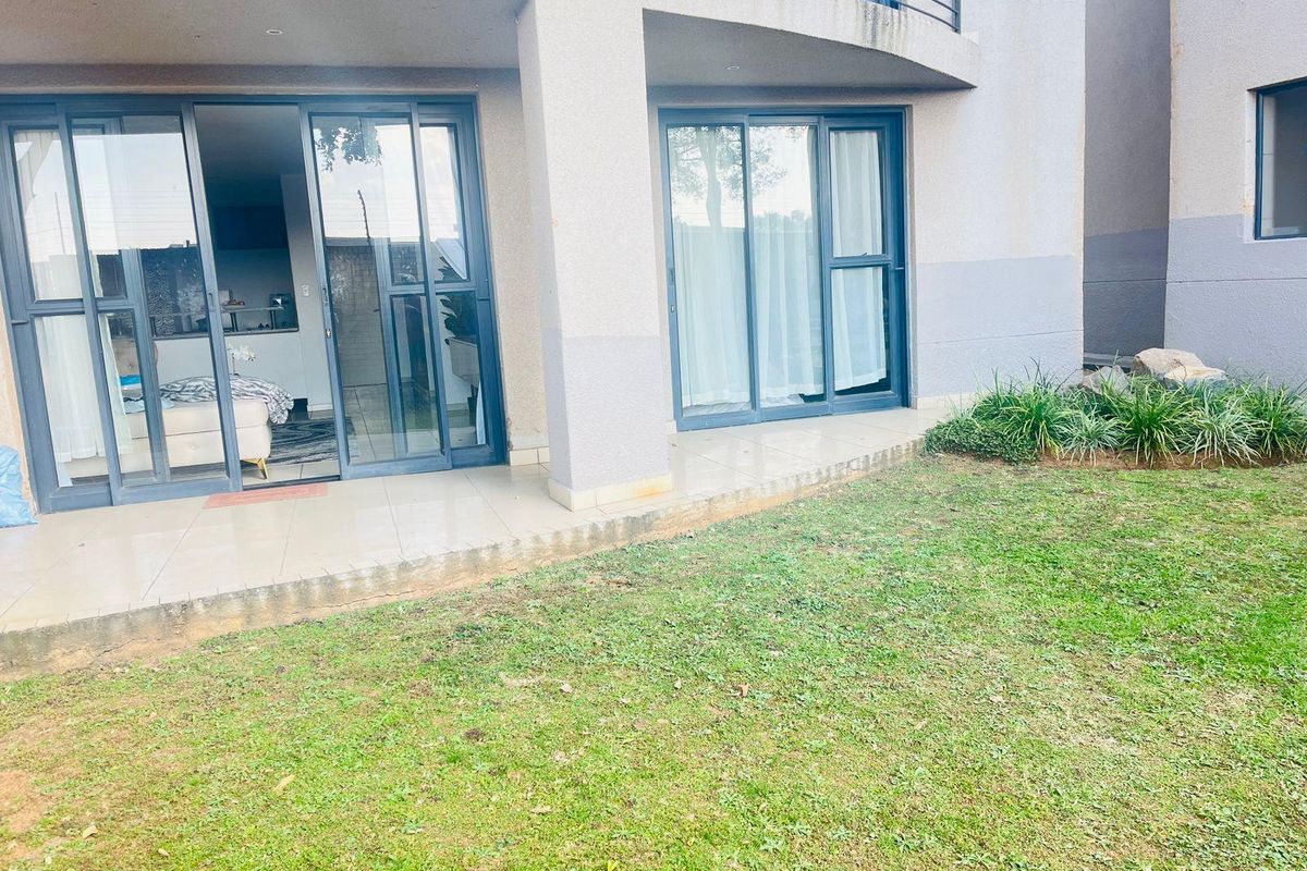 Ground floor apartment exterior featuring a tiled patio area, sliding glass doors, and a private lawn space.