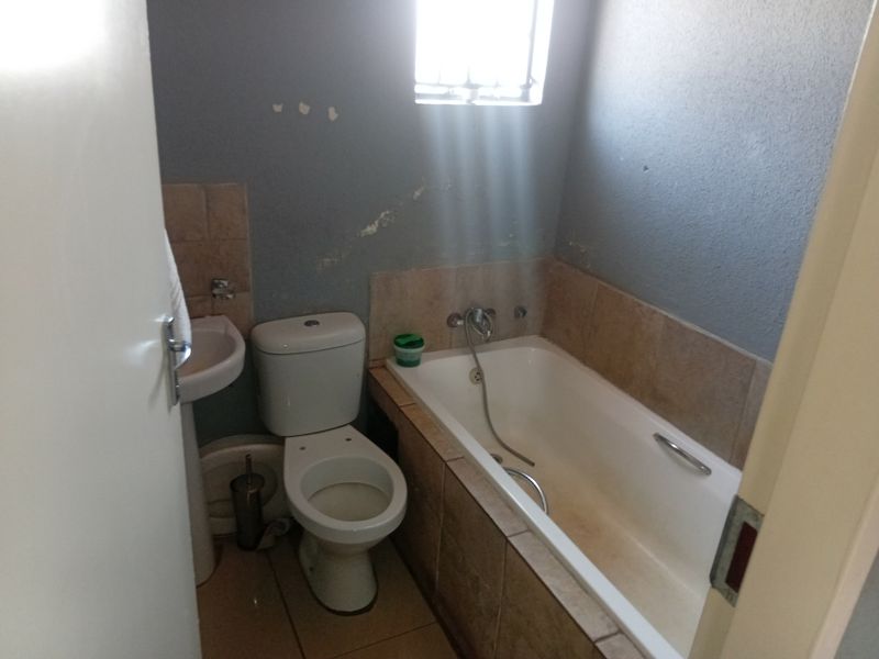 A compact bathroom featuring a pedestal basin, toilet, and a built-in bathtub with tiled surround, requiring cosmetic updates to the wall finishes.