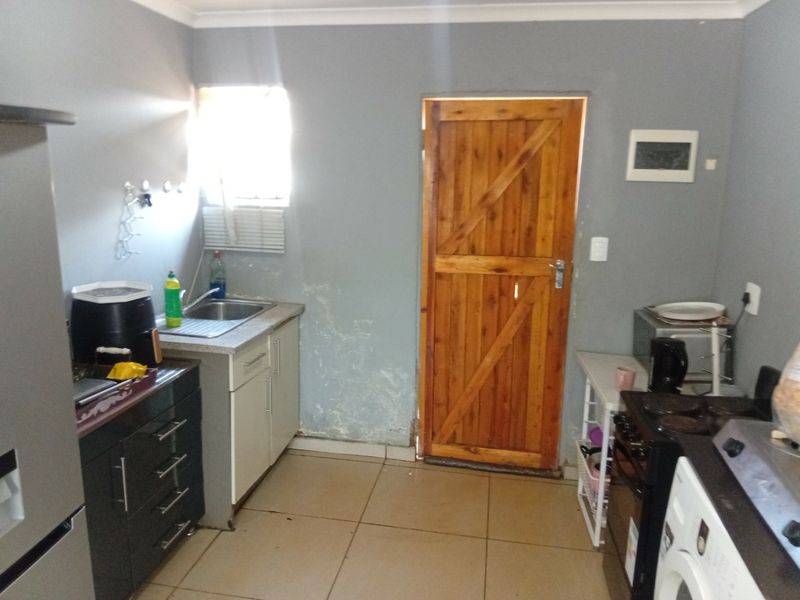 A functional kitchen featuring tiled flooring, dark and light cabinetry, a stainless steel sink, and a wooden exterior door with visible wall surface damage.