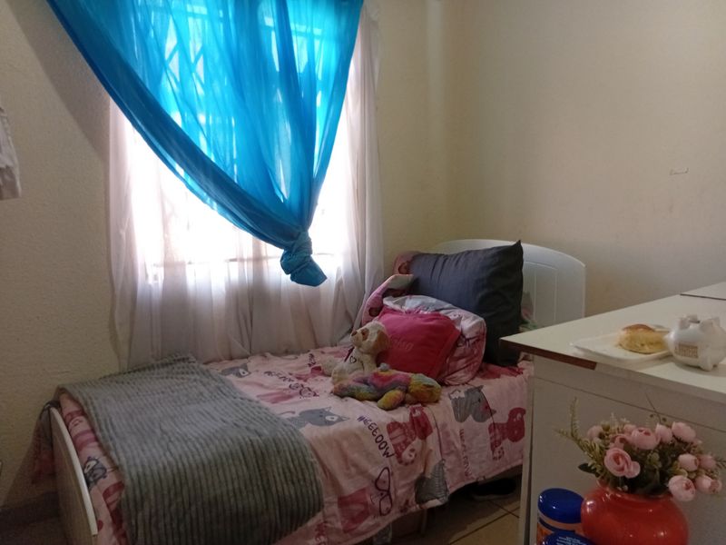 A bedroom featuring tiled flooring and a window fitted with a security gate, providing natural light.