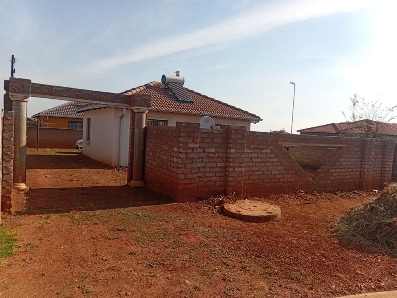 Front view of a residential property featuring a tiled roof with a solar water heater and an unfinished brick boundary wall.