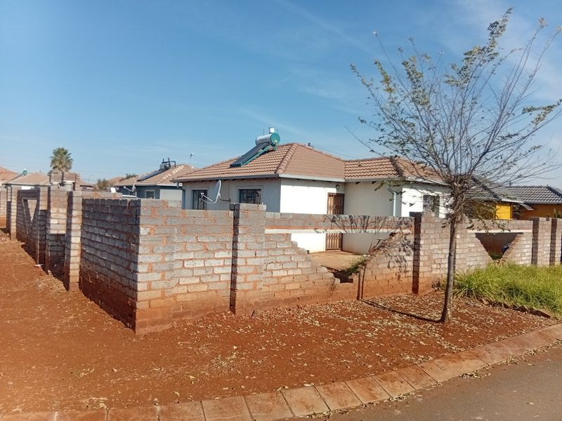 Front view of a single-story house featuring a tiled roof with a solar water heater and an unfinished brick boundary wall.