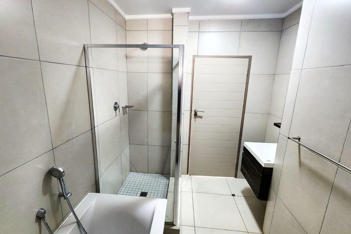 Modern bathroom featuring a glass-enclosed shower, a separate bathtub, and a wall-mounted vanity with neutral floor-to-ceiling tiling.