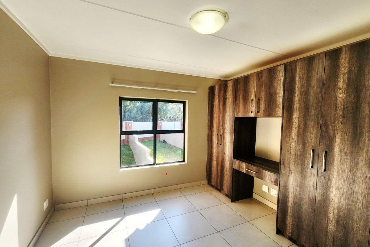 A bright, empty bedroom featuring neutral walls, tiled flooring, and extensive built-in wooden cabinetry with an integrated desk area.