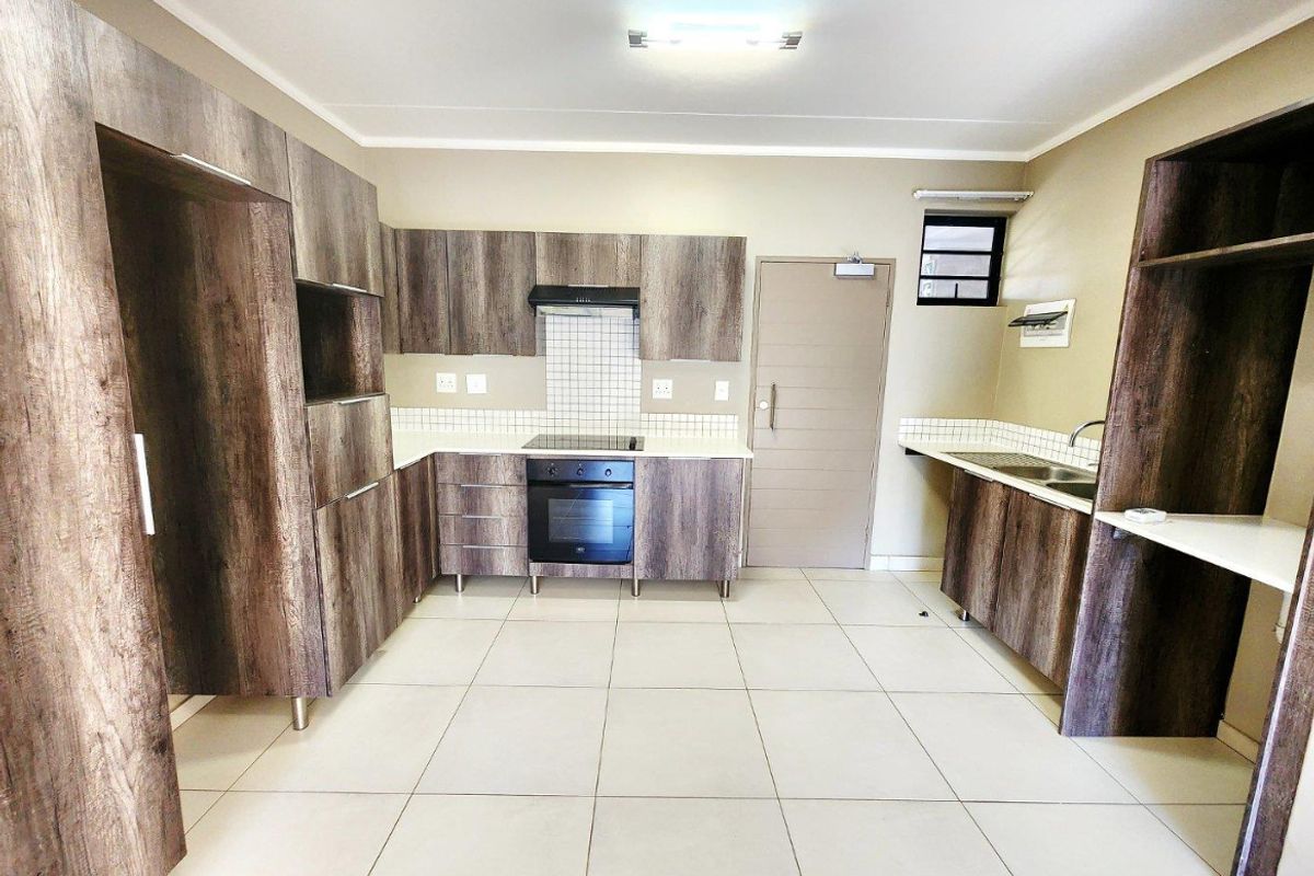 A modern, empty kitchen featuring wood-look cabinetry, built-in oven and hob, tiled backsplash, and neutral floor tiles.