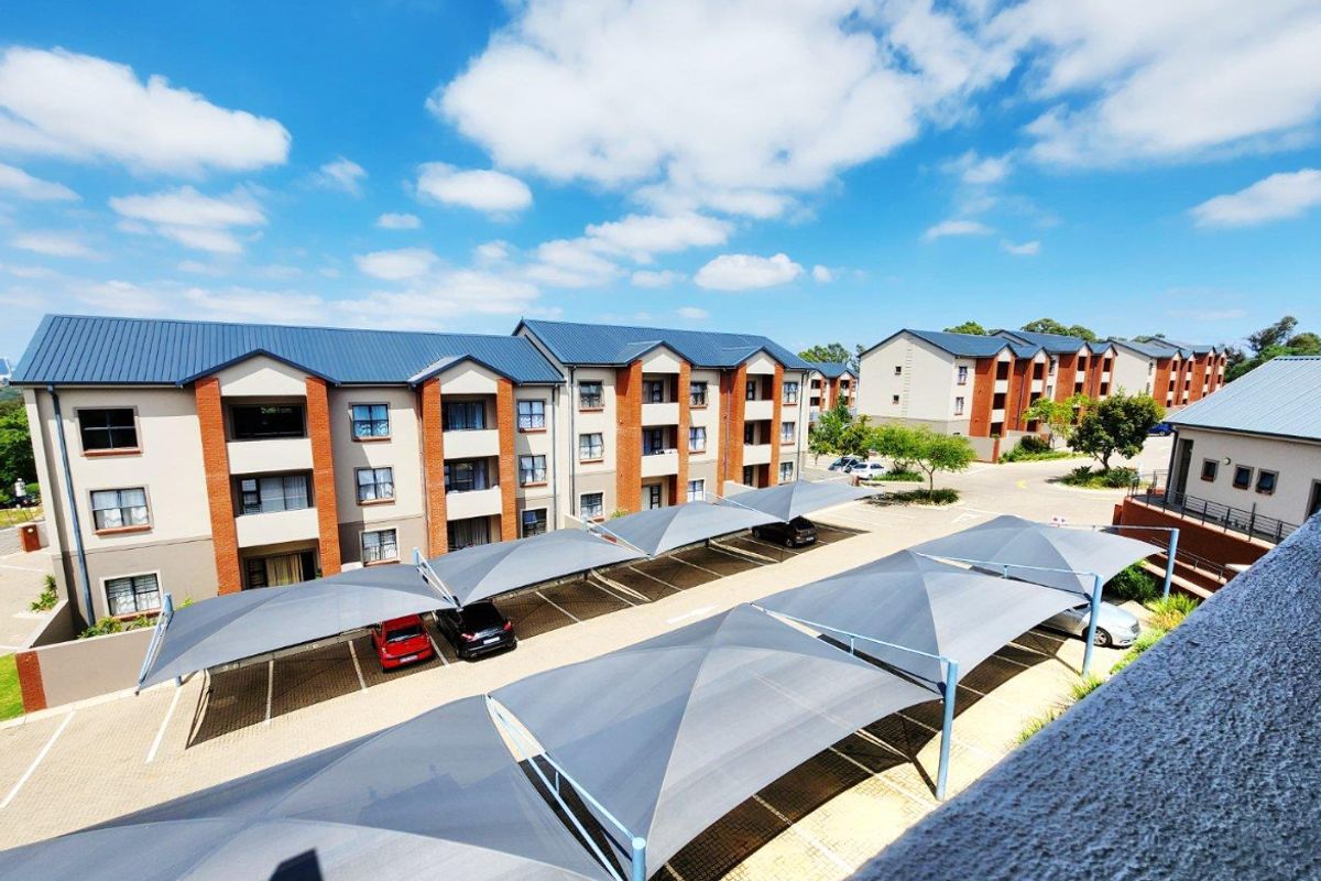 An elevated aerial view of a residential apartment complex featuring multiple buildings with metal roofs and dedicated shaded parking bays.