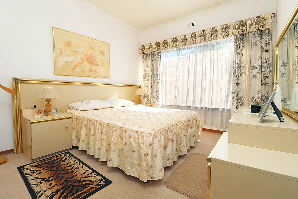 A well-maintained bedroom featuring neutral carpeting, a built-in headboard, and large windows allowing for natural light.