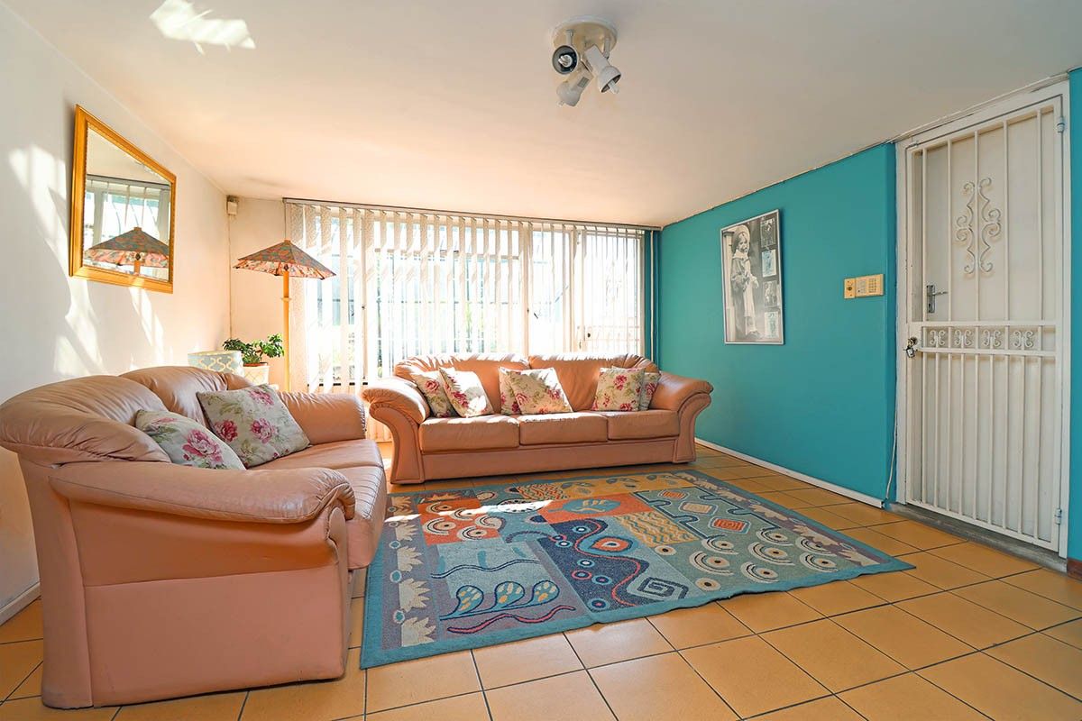 A living room featuring tiled flooring, a security gate at the entrance, and large windows with vertical blinds.