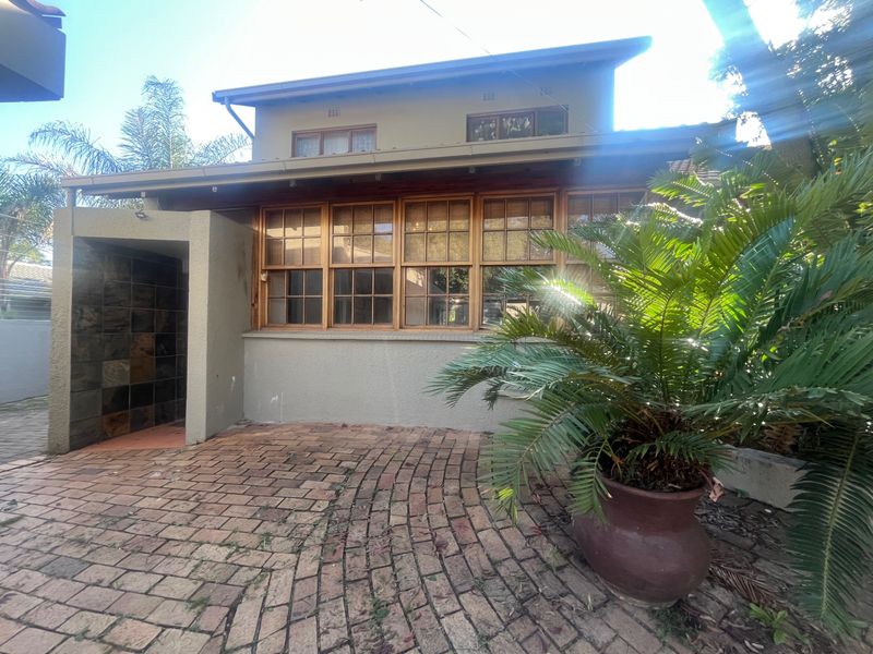 Rear exterior view of the property featuring a brick paved patio area, timber framed windows, and a slate-tiled entrance alcove.