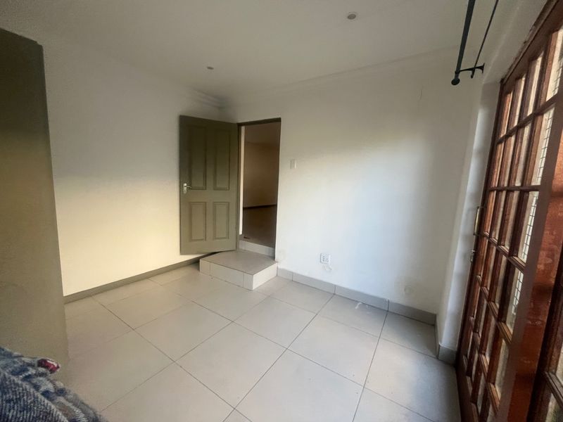 An empty bedroom featuring tiled flooring, recessed downlights, and a timber-framed glass door leading to an outdoor area.