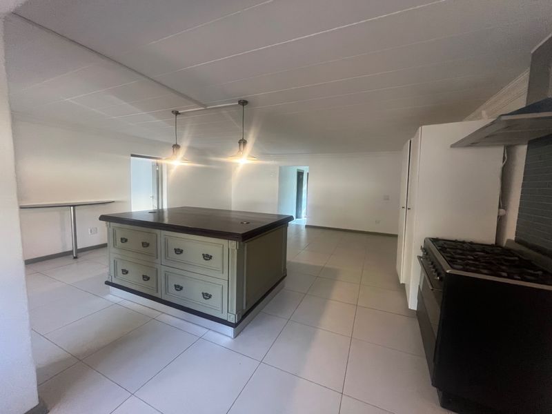 Spacious kitchen featuring a central island with dark wood countertop, gas stove with extractor, and neutral tiled flooring throughout.