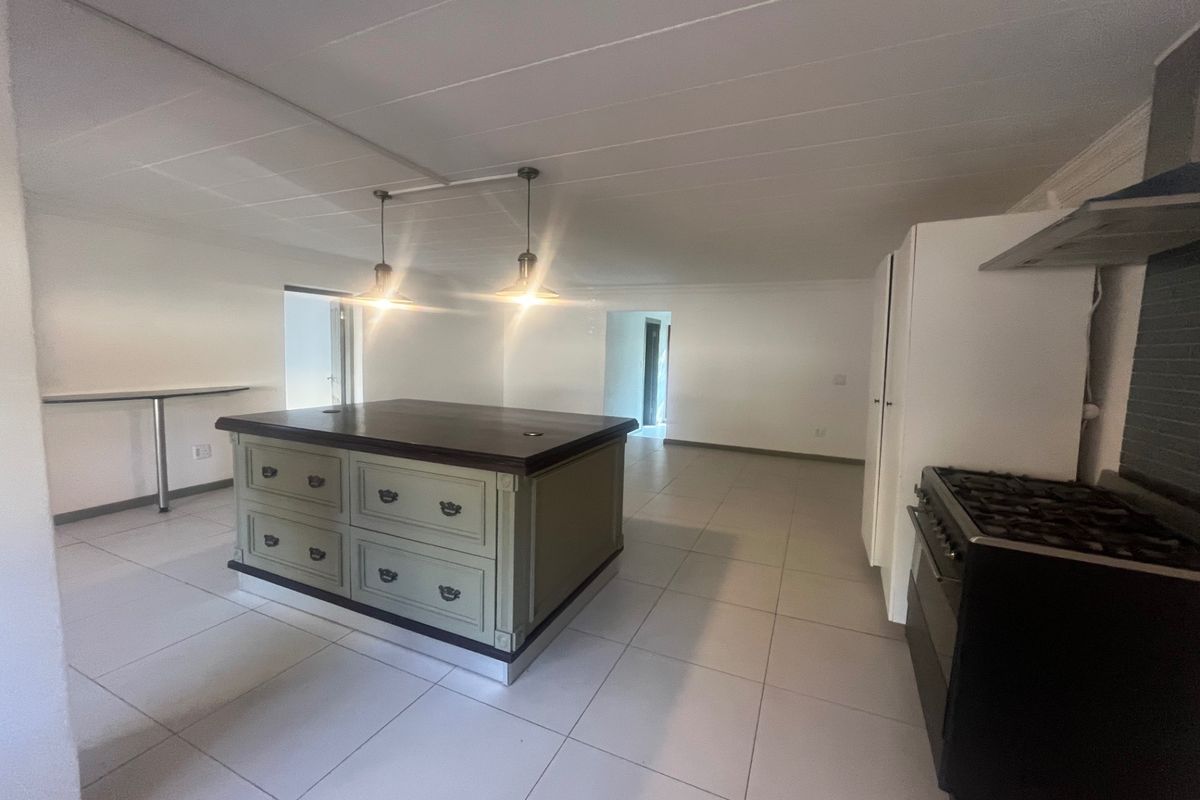 Spacious kitchen featuring a central island with dark wood countertop, gas stove with extractor, and neutral tiled flooring throughout.