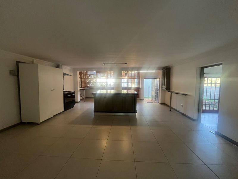 Spacious open-plan kitchen area featuring a central island, built-in oven, extractor fan, and neutral tiled flooring, offering a versatile layout for living and dining.
