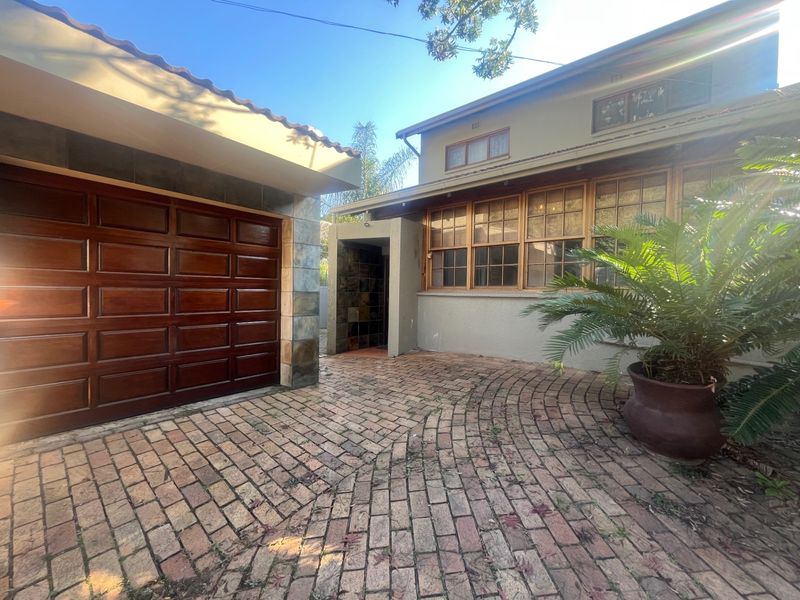 Front exterior view of the property featuring a brick paved driveway, a wooden garage door, and stone cladding accents.
