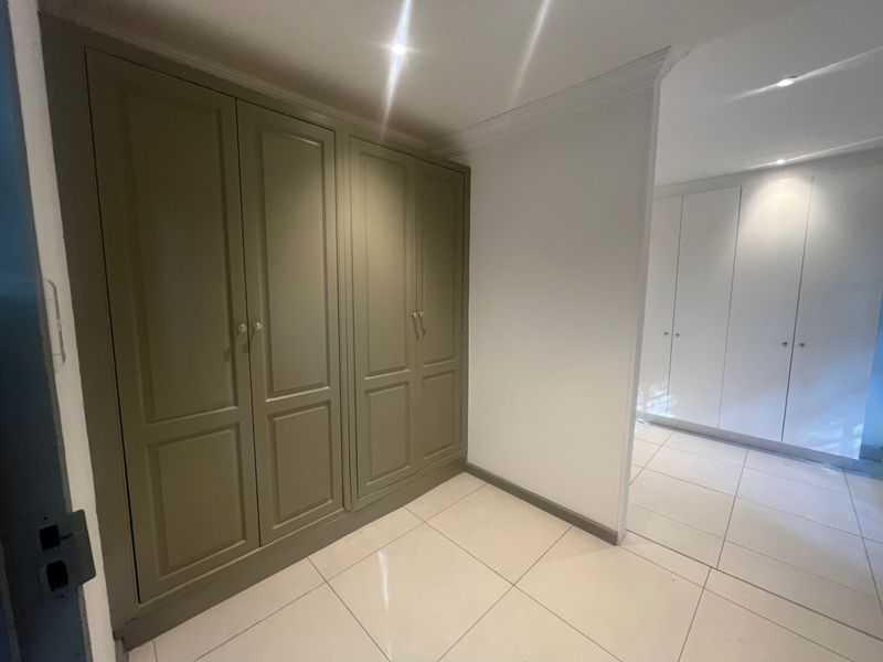 A bright hallway featuring extensive built-in cabinetry, neutral tiled flooring, and recessed downlighting, providing ample storage space.