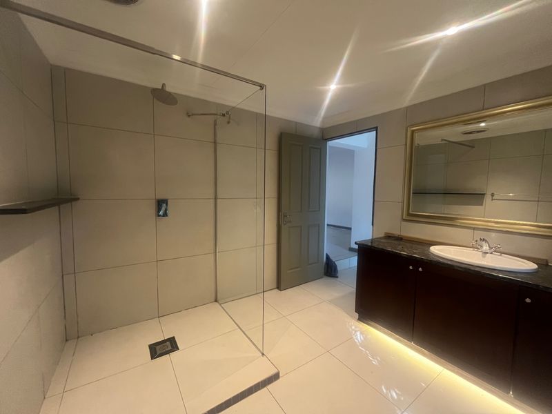 Modern bathroom featuring a spacious walk-in shower with glass screen, dark wood vanity cabinet with granite countertop, and neutral wall and floor tiling.