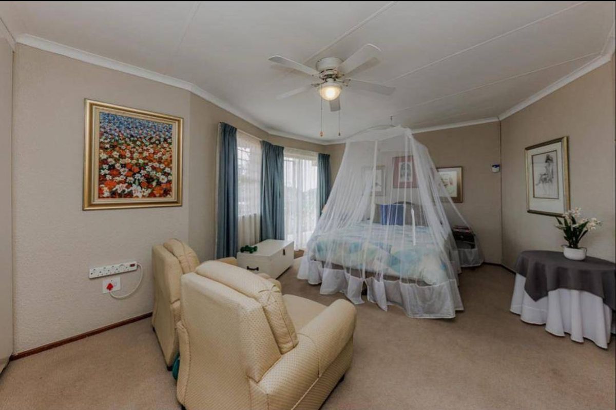 A spacious bedroom featuring neutral wall tones, carpeted flooring, a ceiling fan, and a sliding glass door providing access to the exterior.