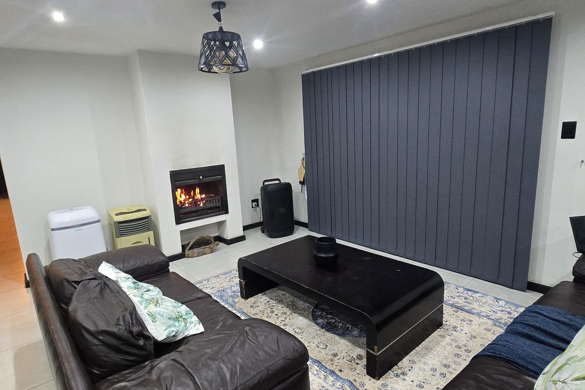 A comfortable living room featuring a built-in fireplace, tiled flooring, and large vertical blinds, creating a cozy and functional space.