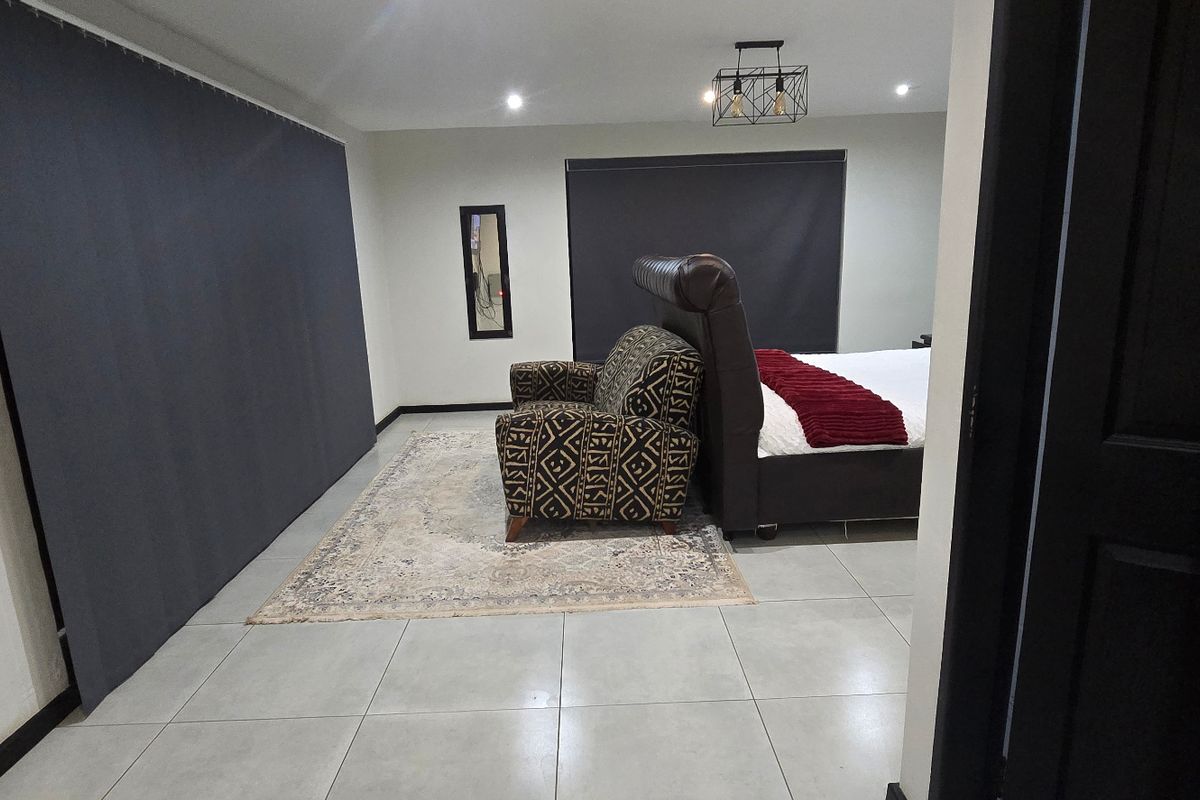 A spacious bedroom featuring neutral tiled flooring, recessed downlighting, and modern roller blinds, offering a clean and functional living space.