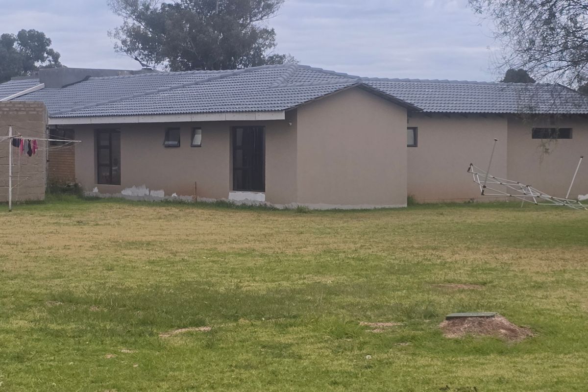 Rear view of a single-story house featuring a tiled roof and plastered exterior walls, set on a large grassed plot.