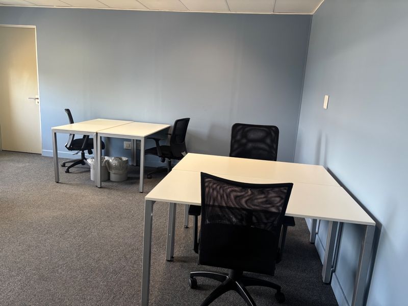 A functional commercial office space featuring neutral blue walls, carpeted flooring, and a suspended ceiling, suitable for a professional work environment.