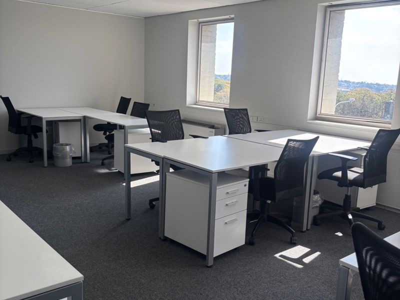 A bright, functional commercial office space featuring carpeted flooring, suspended ceiling tiles, recessed lighting, and large windows providing natural light.