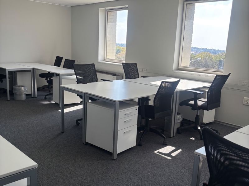 A functional commercial office space featuring carpeted flooring, suspended ceiling tiles with recessed lighting, and large windows providing natural light.