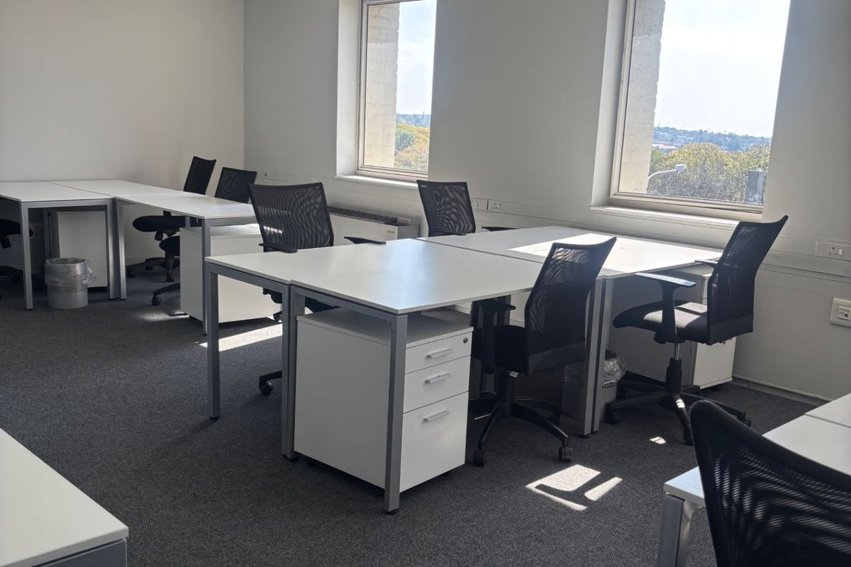 A functional commercial office space featuring carpeted flooring, suspended ceiling tiles with recessed lighting, and large windows providing natural light.