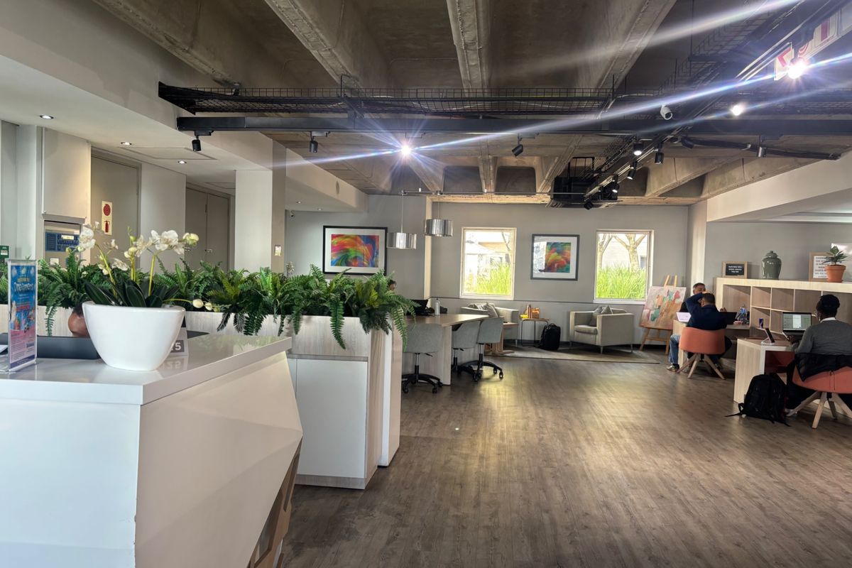 Modern open-plan commercial office space featuring exposed concrete ceilings, track lighting, and durable laminate flooring with integrated reception and storage areas.