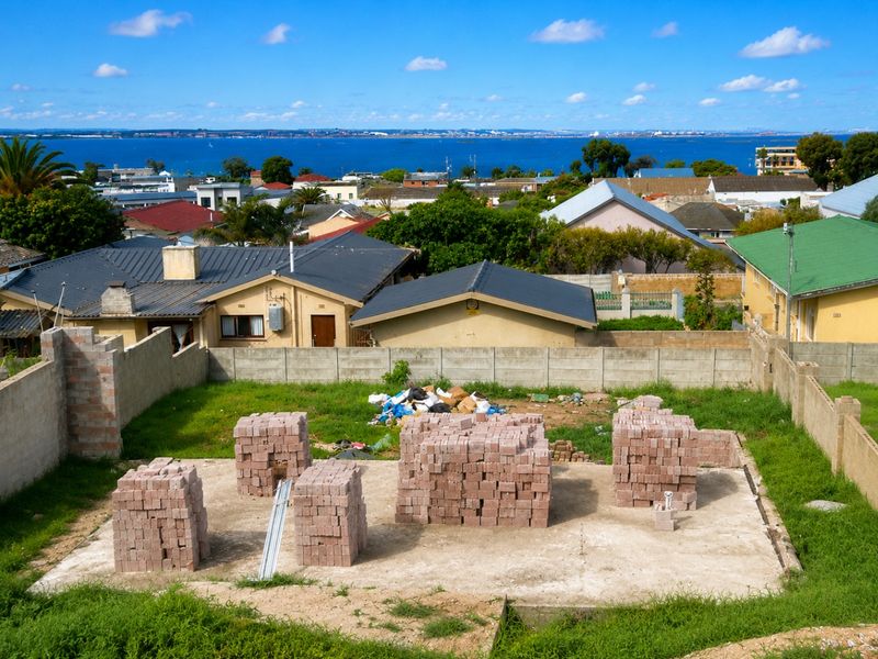 Vacant residential plot featuring a concrete foundation slab with stacked building bricks, enclosed by perimeter boundary walls with views of the surrounding neighborhood.