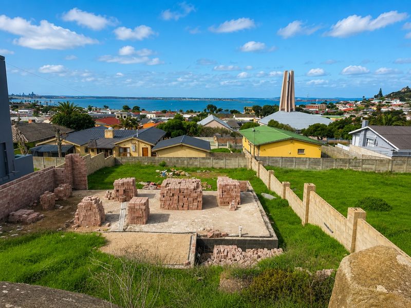 Vacant residential land featuring an established concrete foundation and stacks of construction bricks, offering scenic coastal and neighbourhood views.