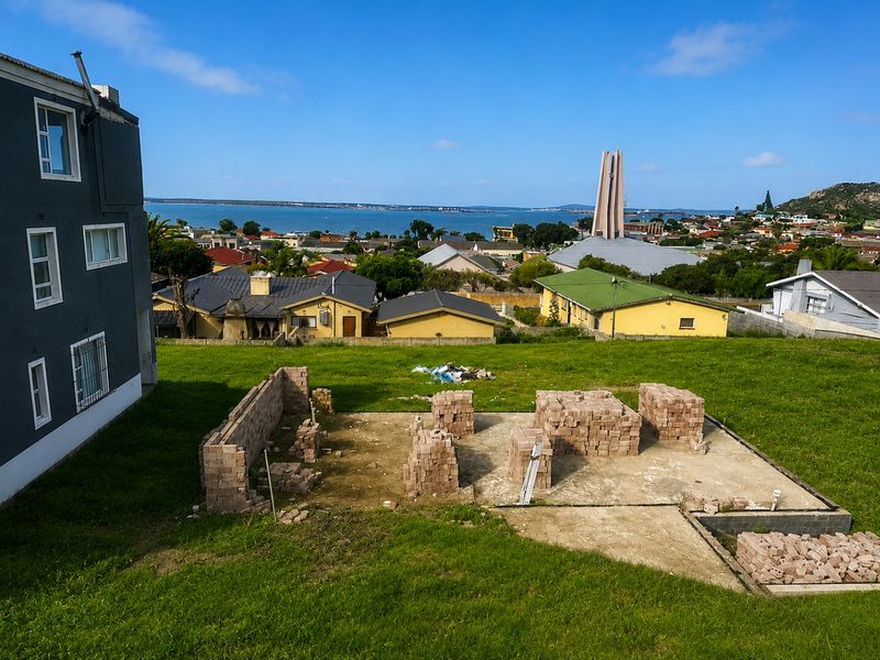 A vacant residential plot featuring an incomplete brick foundation and construction materials, offering elevated views of the surrounding neighborhood and coastal landscape.