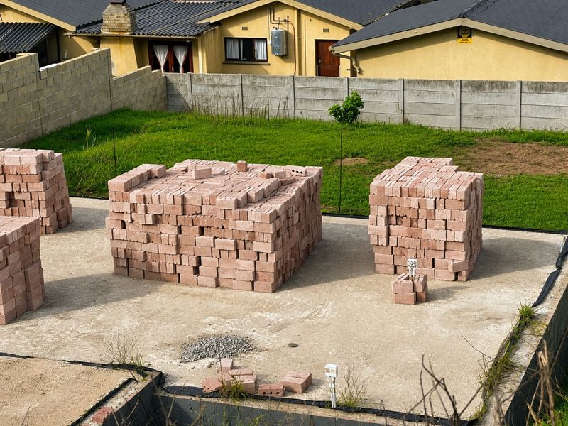 A view of a residential construction site featuring a concrete foundation slab with stacks of red clay bricks ready for building.