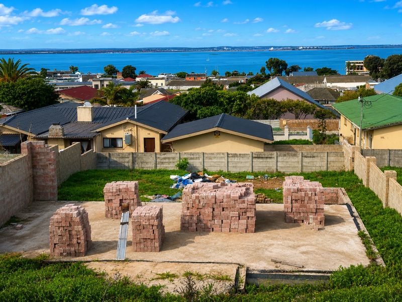 Vacant residential plot featuring a concrete foundation slab and stacked building materials, offering scenic coastal and neighborhood views.