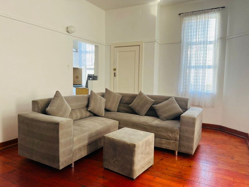 A living room featuring original hardwood flooring, picture rails, and a view through to the kitchen area.