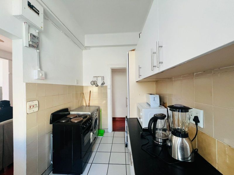 Compact kitchen featuring white cabinetry, black countertops, tiled backsplash, and tiled flooring, equipped with a built-in electric stove.