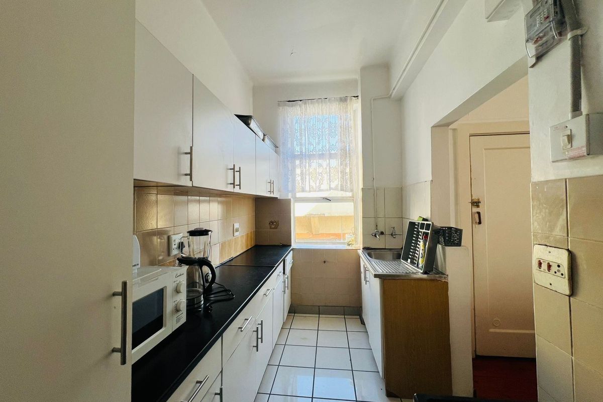 A functional galley-style kitchen featuring white cabinetry, dark laminate countertops, tiled flooring, and a window providing natural light.
