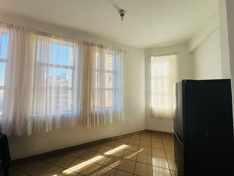 A bright, empty living area featuring ceramic tile flooring and large windows that allow for ample natural light.
