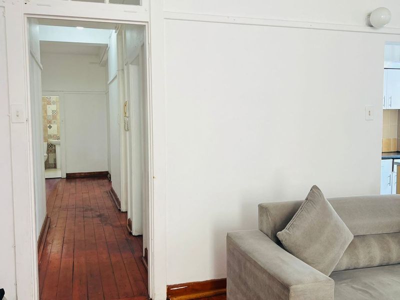 A living area featuring original timber flooring and a classic doorway with a transom window, leading into a hallway.