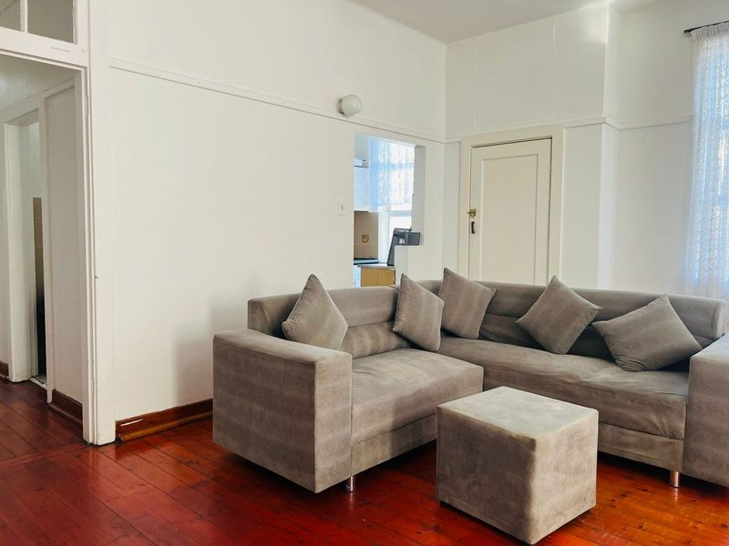 A living room featuring original hardwood flooring, picture rails, and a convenient pass-through window connecting to the adjacent kitchen area.