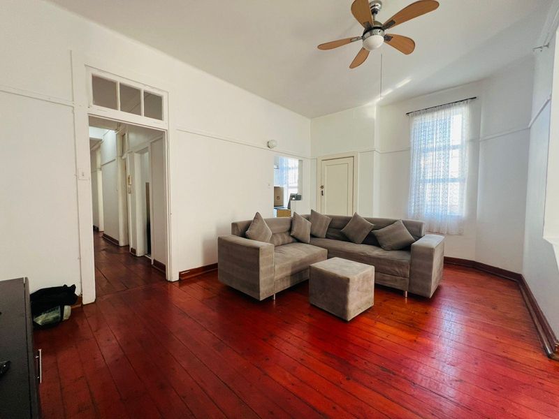 A living room featuring original hardwood flooring, a ceiling fan, and classic architectural details including picture rails and a transom window above the doorway.