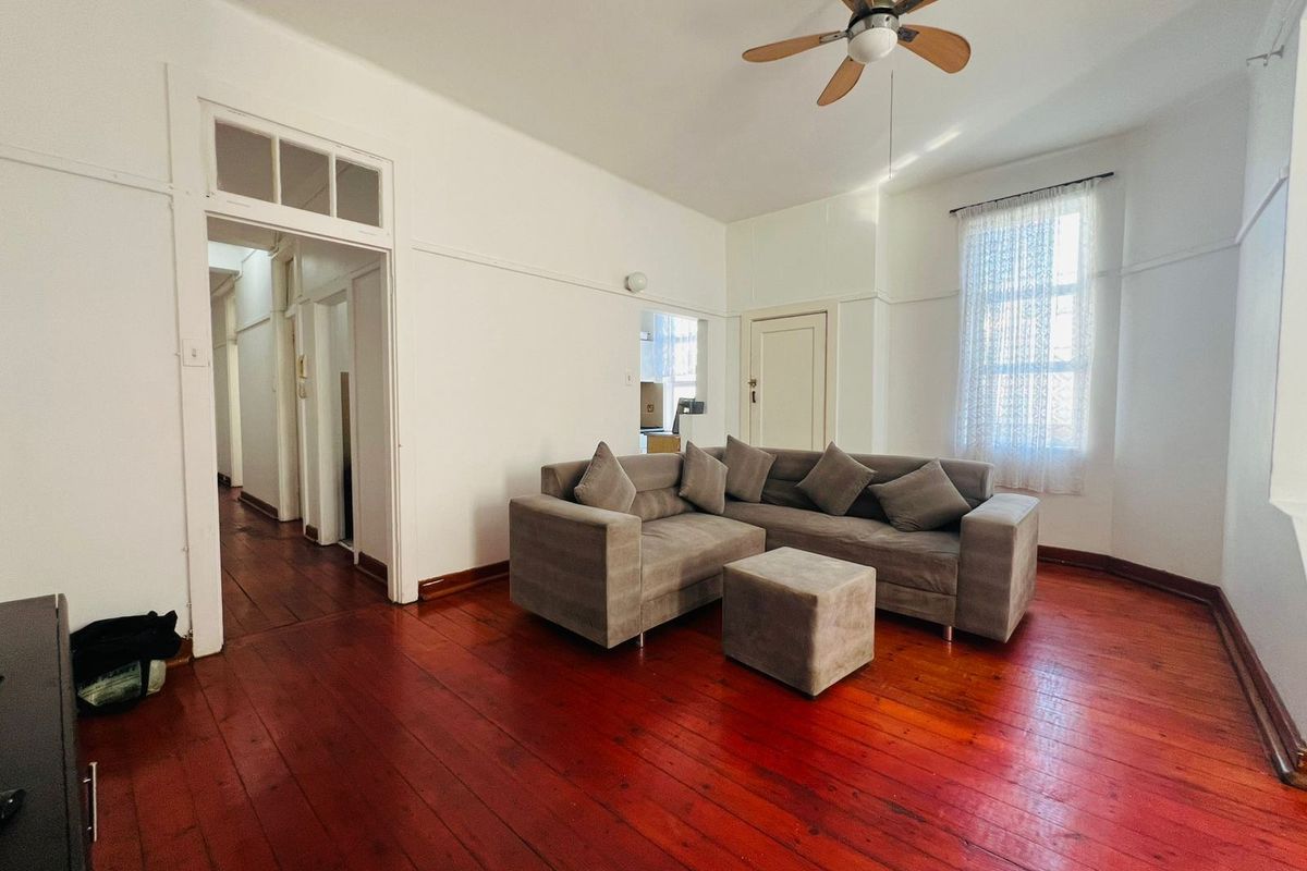 A living room featuring original hardwood flooring, a ceiling fan, and classic architectural details including picture rails and a transom window above the doorway.