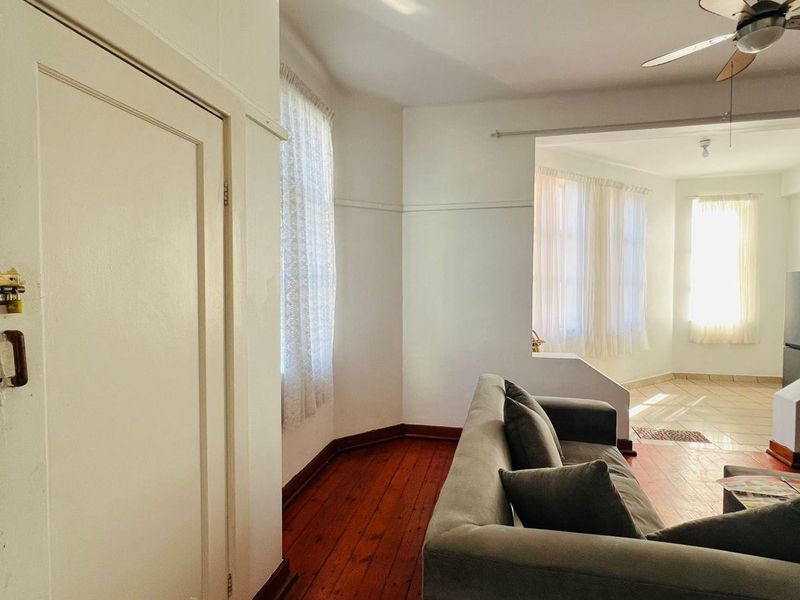 Living area featuring original hardwood flooring, a ceiling fan, and a transition to a tiled space, offering a classic layout with potential for modernization.