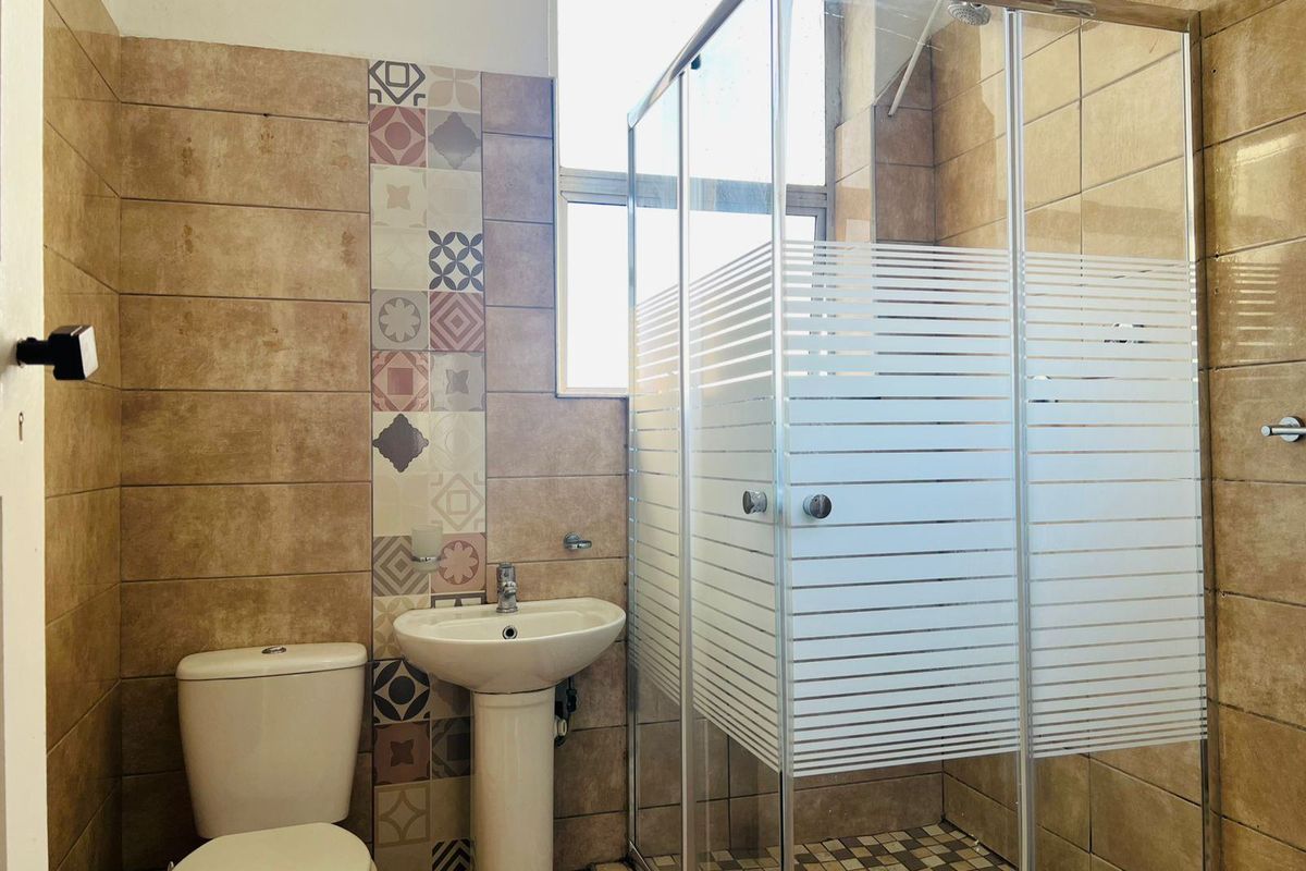A functional bathroom featuring a pedestal basin, a glass shower enclosure, and decorative ceramic wall tiling.