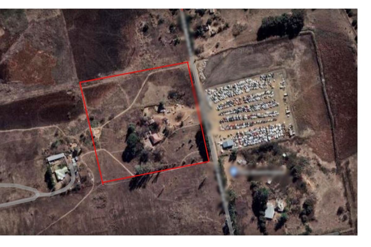 Aerial view of a vacant residential land plot with defined boundaries, showing surrounding terrain and access road.