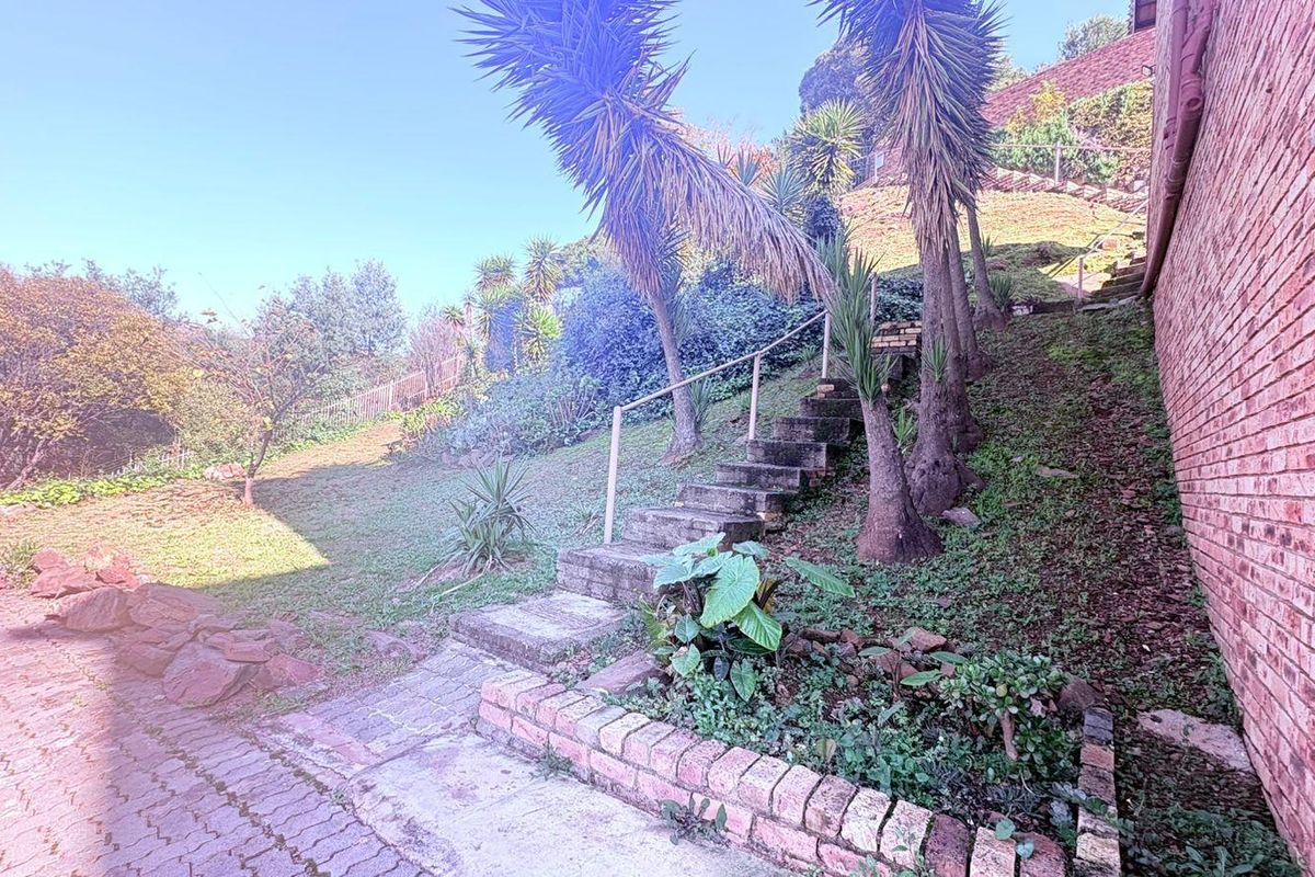 Rear exterior view featuring a brick retaining wall, concrete staircase with metal handrail, and sloped garden area leading up the property.